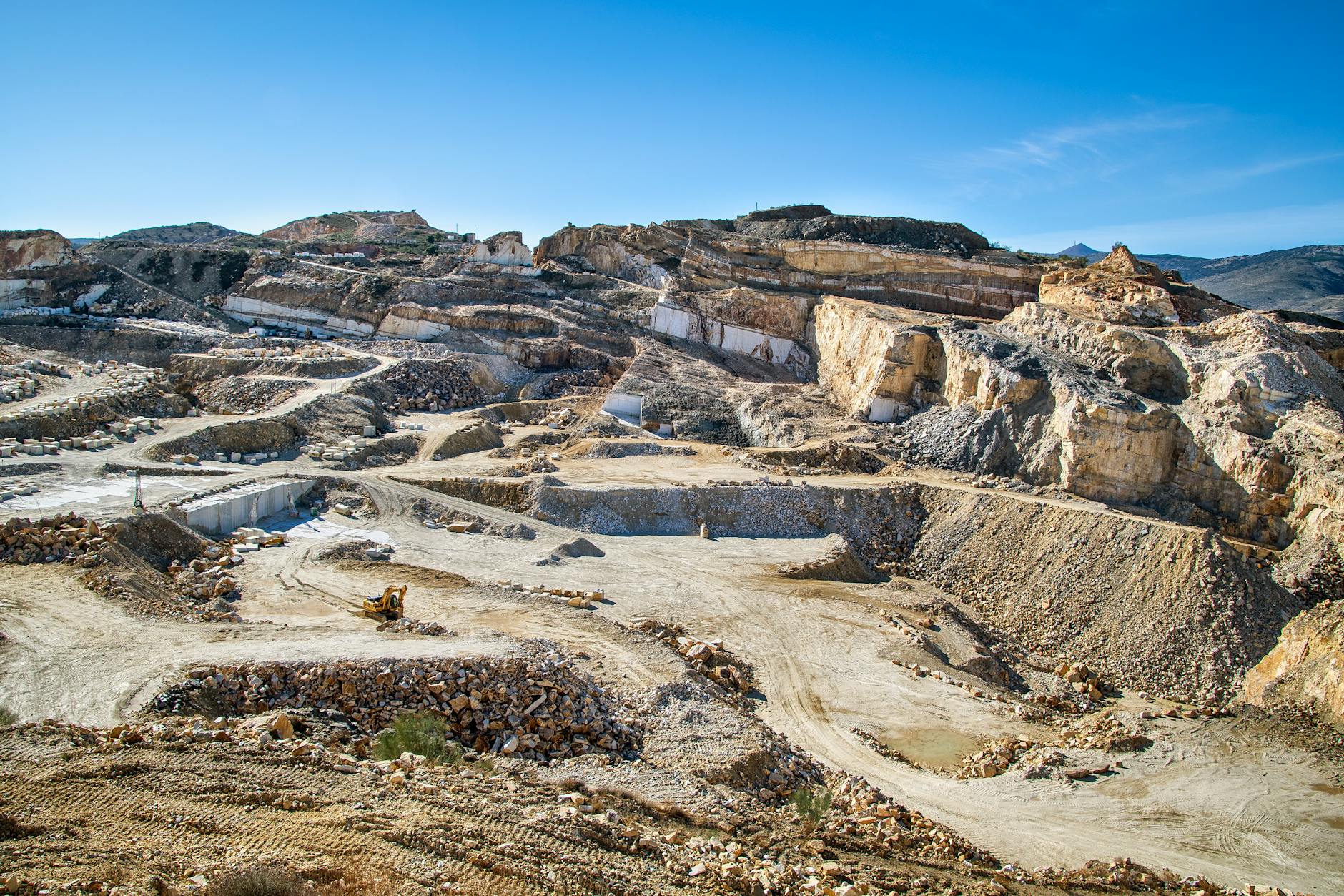 Kopalnia odkrywkowa z warstwami skał i pracującymi maszynami budowlanymi