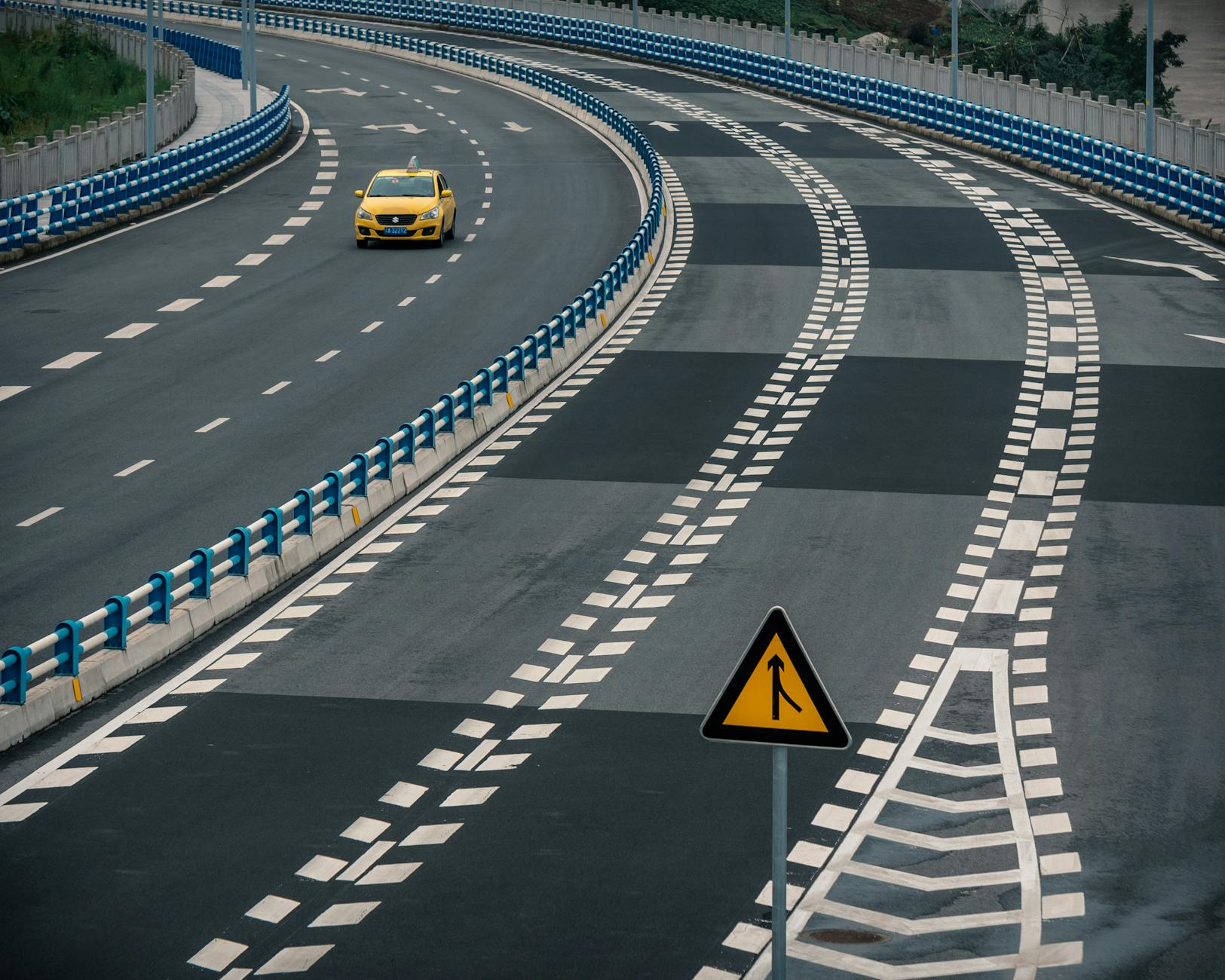 Żółta taksówka jedzie pustą, zakręconą autostradą z znakiem włączenia się