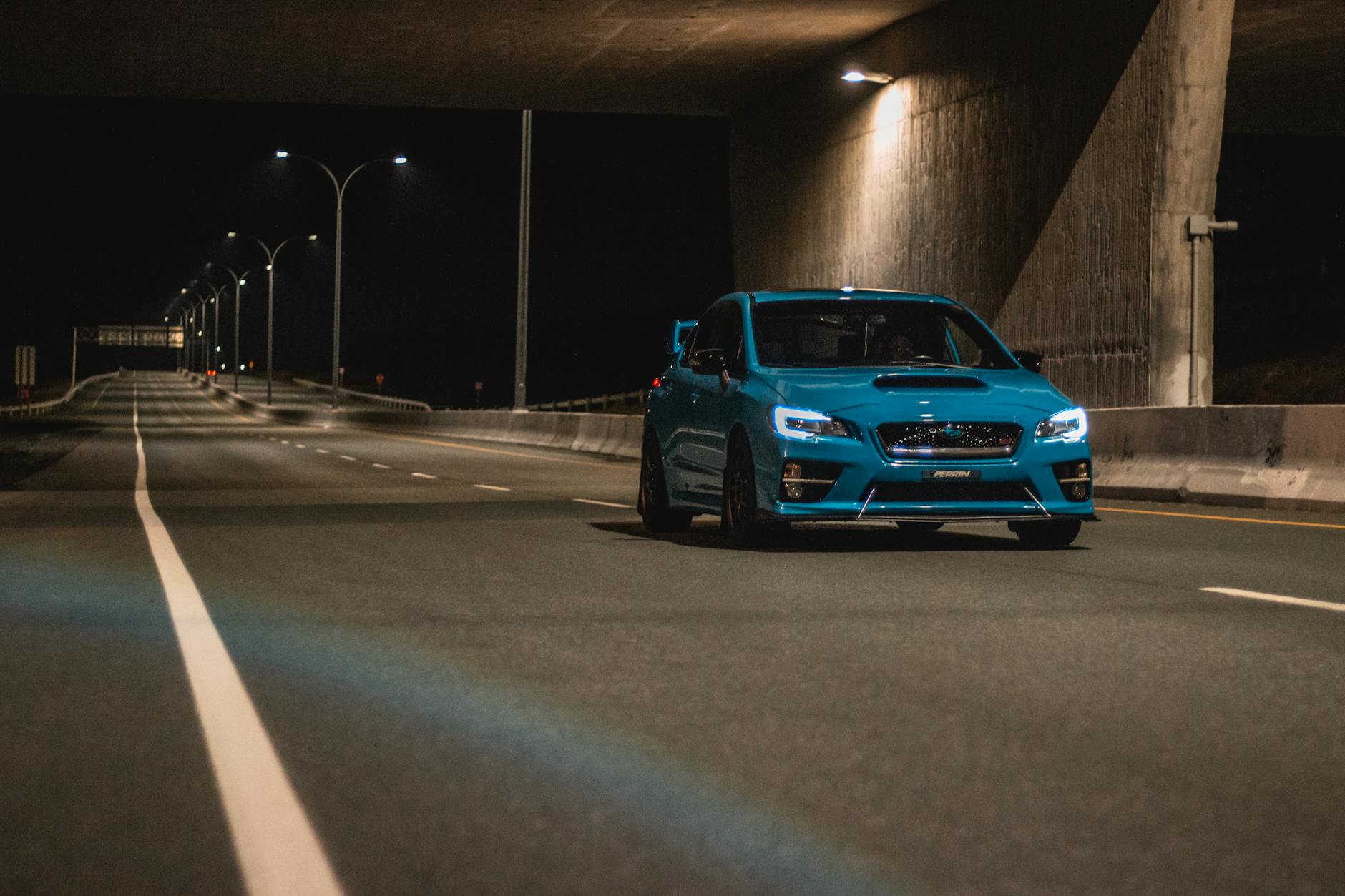 Niebieskie sportowe auto nocą na pustej trasie w warszawskim tunelu