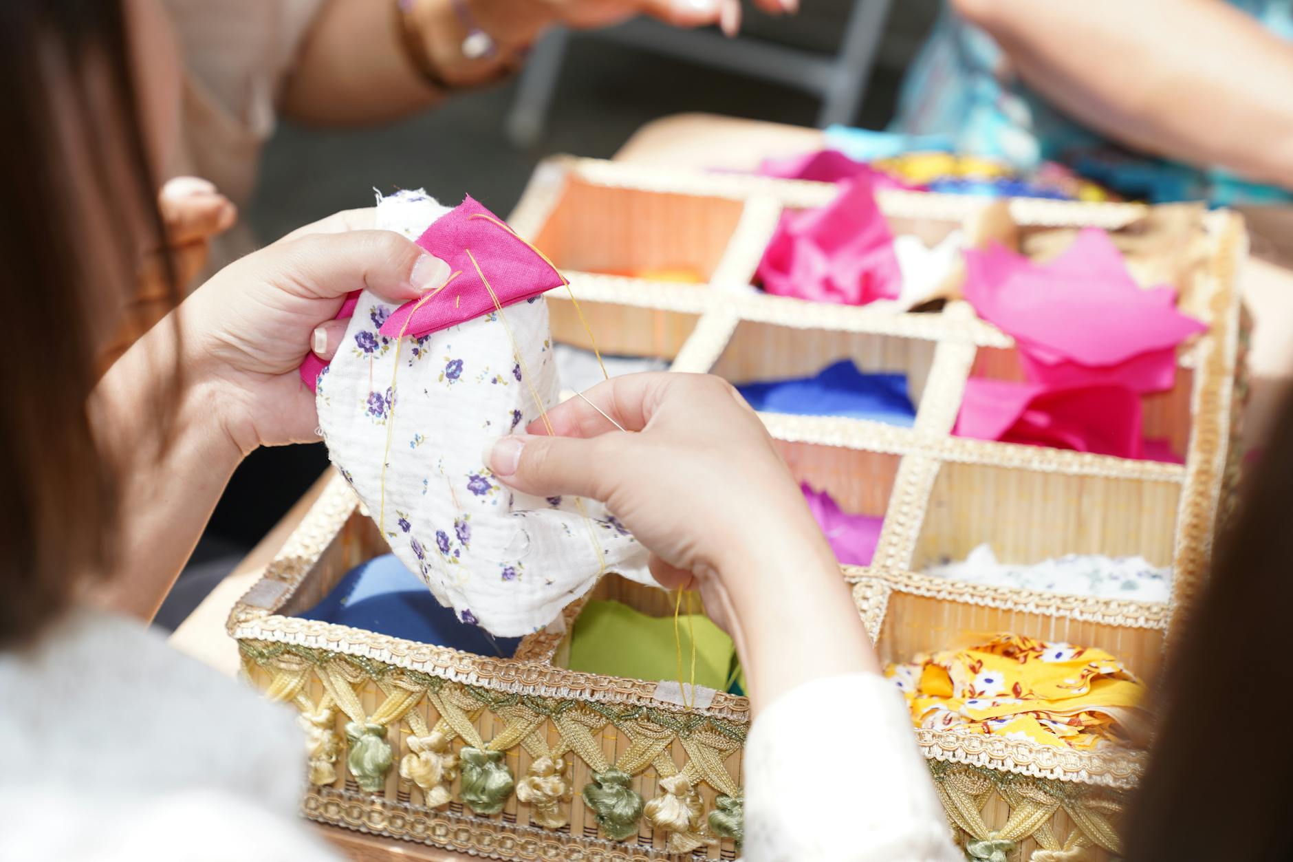 Jak zacząć szyć patchwork: praktyczny poradnik dla początkujących Dłonie szyjące kolorowy patchwork, obok pudełko z barwnymi skrawkami