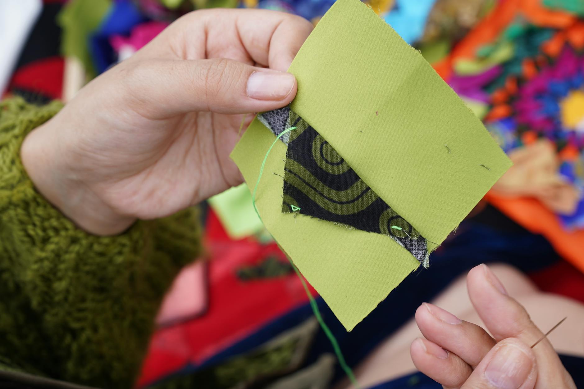 Dłonie zszywające kolorowe kawałki materiału techniką patchworku