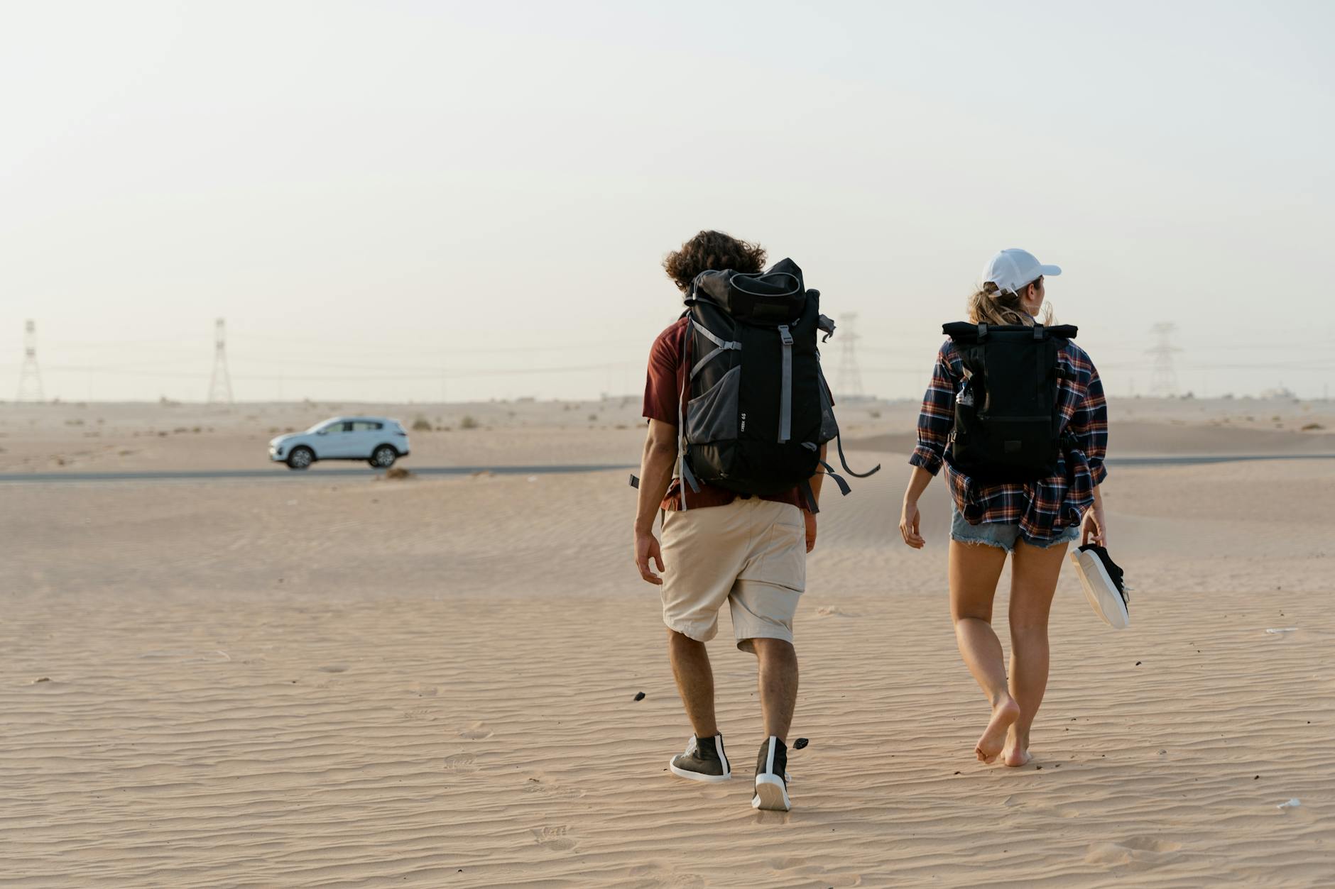 Para z plecakami idąca przez rozległą pustynię ku horyzontowi