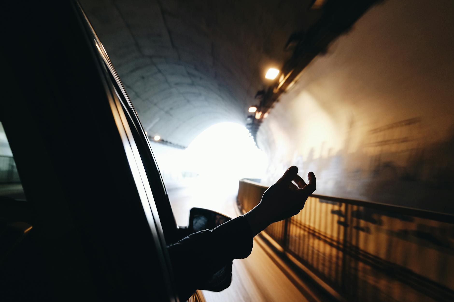 Ręka wystawiona z okna jadącego auta w jasno oświetlonym tunelu