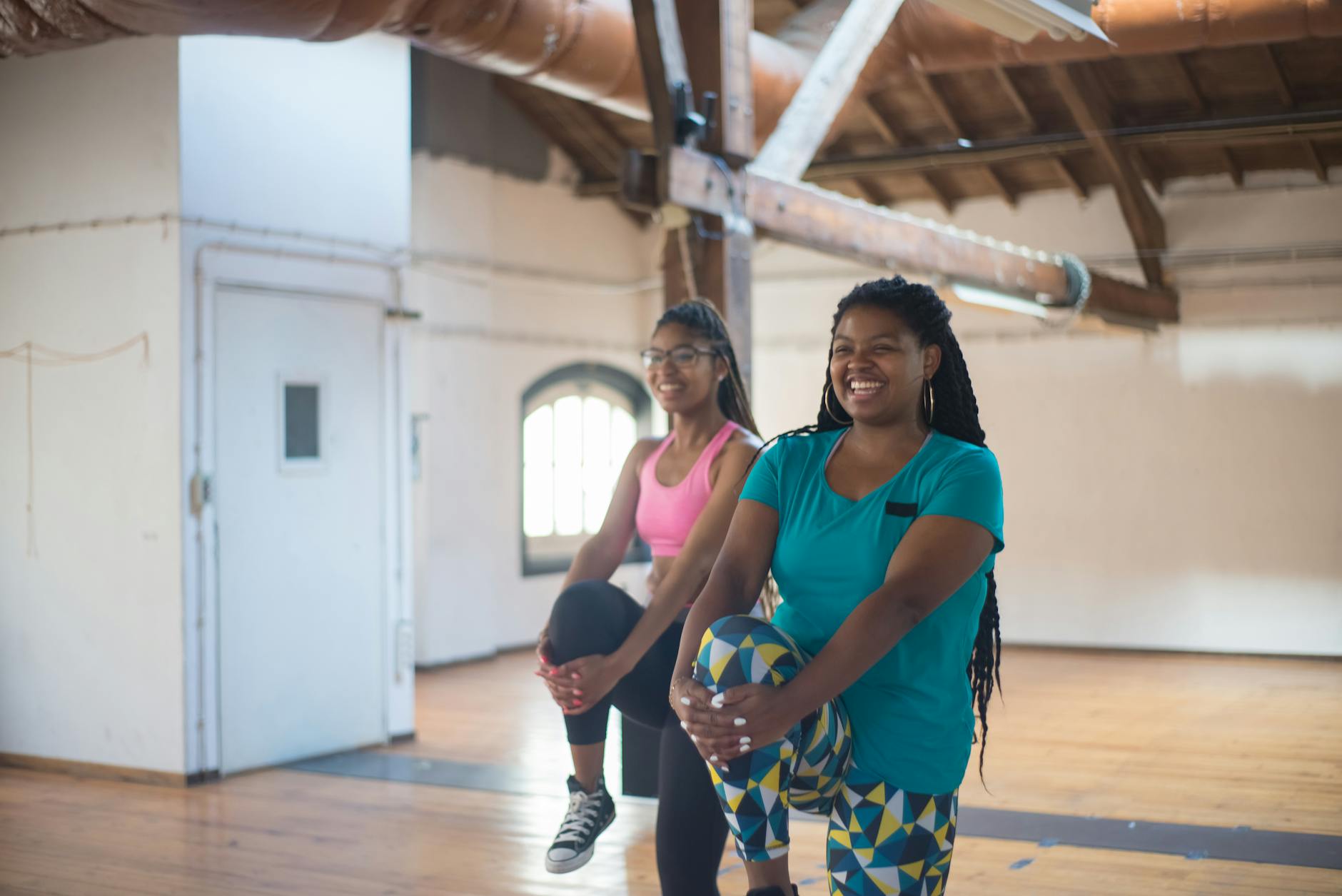 Dwie uśmiechnięte kobiety rozciągają się w jasnym studio fitness