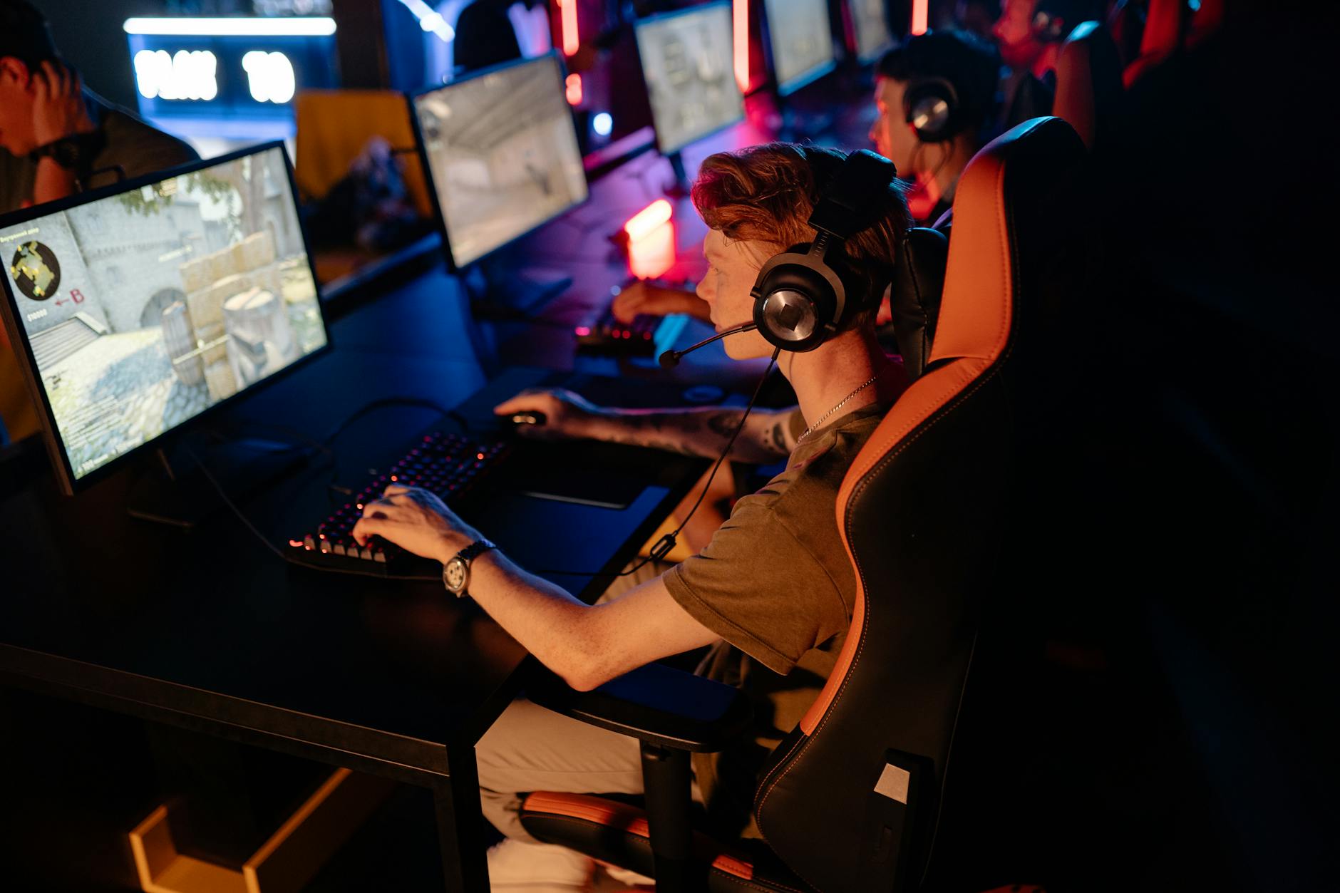 Gracze e-sportowi skoncentrowani przy komputerach w ciemnej arenie