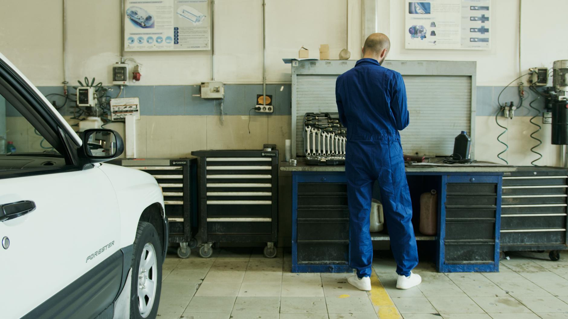 Mechanik w niebieskim kombinezonie sprawdza białą Toyotę w warsztacie