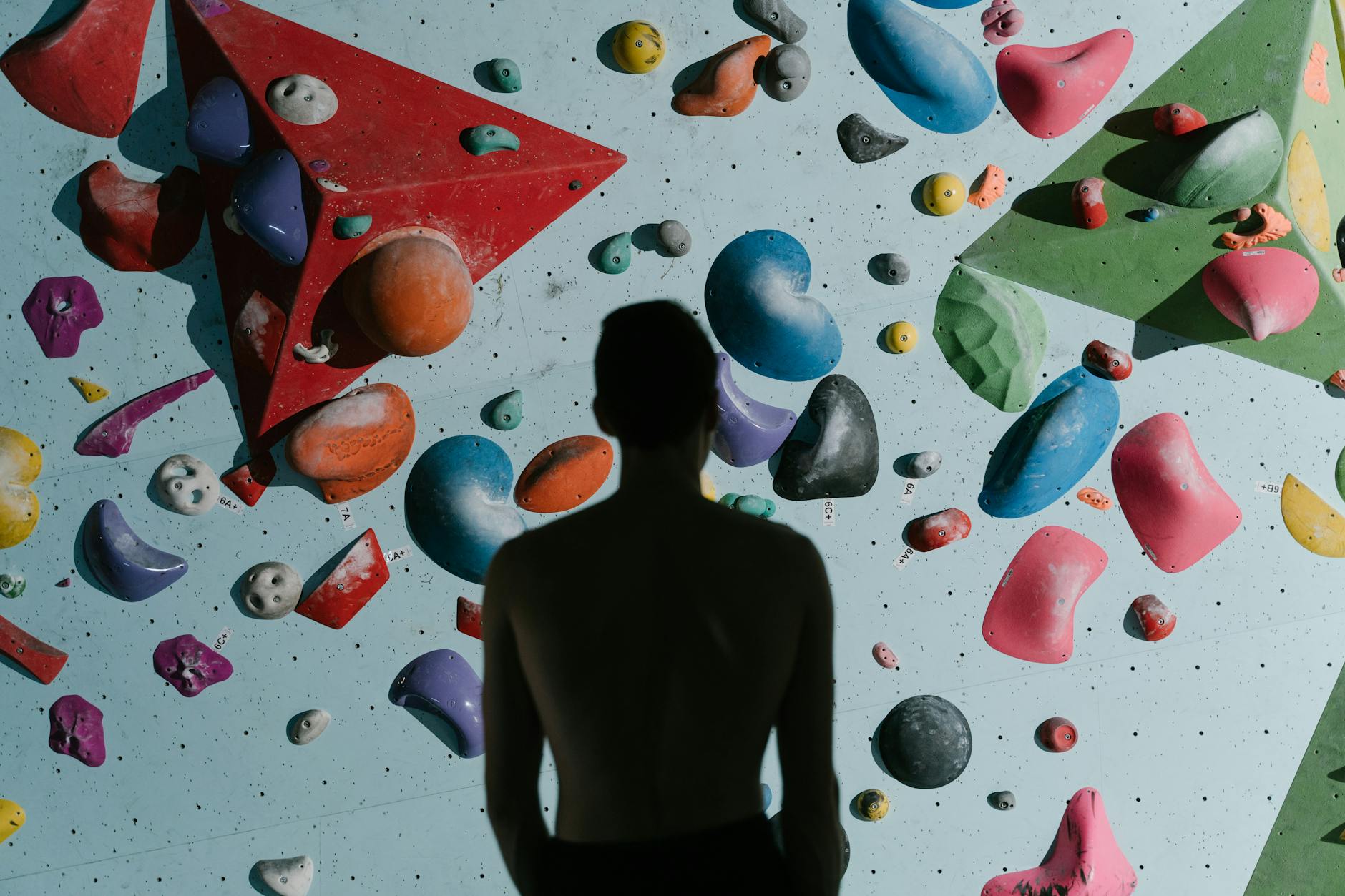Sylwetka mężczyzny przed kolorową ścianką boulderową w hali Sylwetka mężczyzny przed kolorową ścianką boulderową w hali